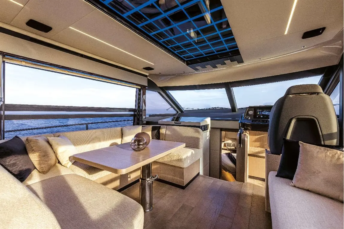Luxurious boat interior featuring seating, a dining table, and panoramic windows overlooking calm waters.